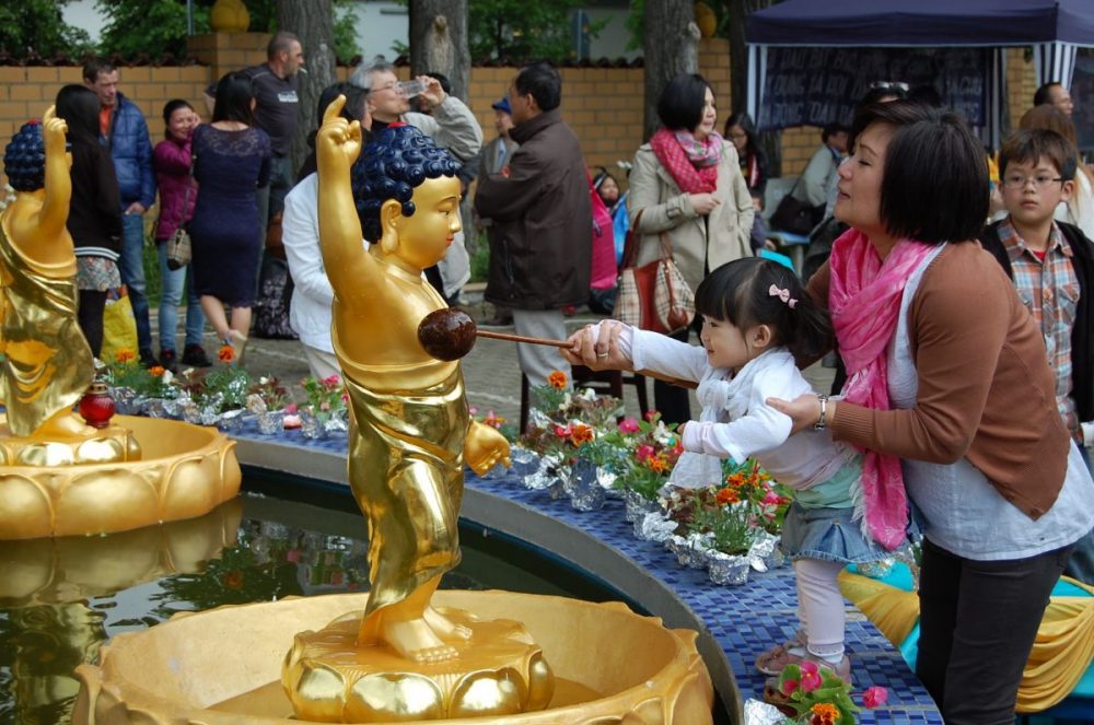 Pagode Vien Giac Hannover, eine Mutter hält ihr Kleinkind hoch, damit es mit einer Kelle eine Kinderstatue von Buddha mit Wasser übergießt.
